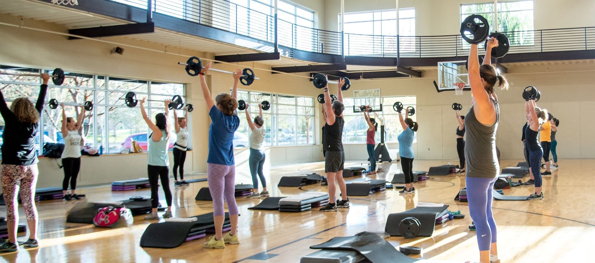 Group fitness class lifting barbells inside the bright gymnasium at Hawthorn Farm Athletic Club in Hillsboro, Oregon, featured on the Choose Your Savings slider.