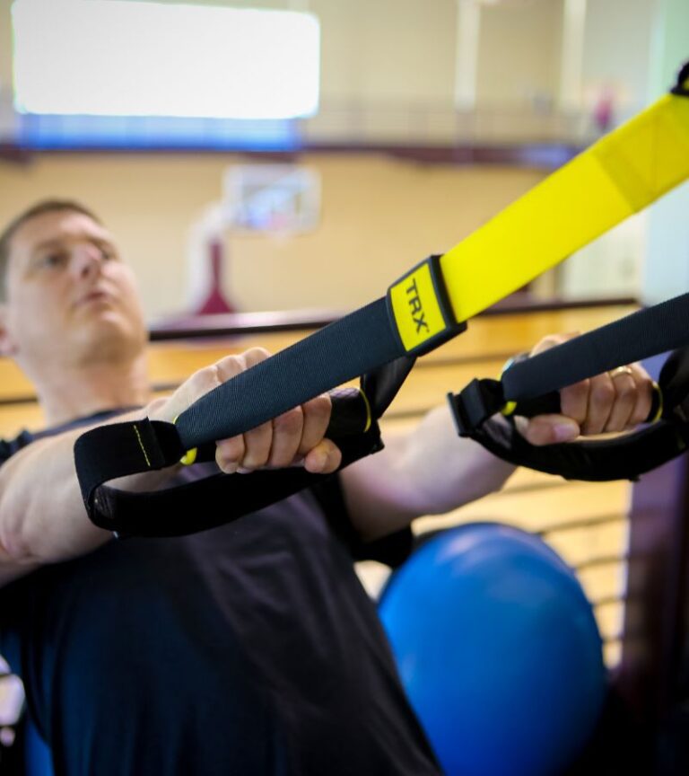 Member using TRX suspension straps inside Hawthorn Farm Athletic Club in Hillsboro, Oregon, demonstrating functional and circuit training options.